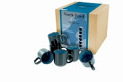 6-teiliges Tassen-Set „Nordic Fjord Blue“ aus hochwertigem Steingut in Dunkelgrau mit blau gesprenkelter Innenlasur, mit Produktkarton im Hintergrund; Ansicht schräg von vorn in leichter Draufsicht