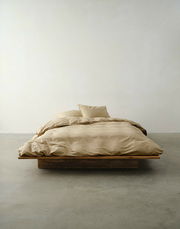 Beige Bettwäsche auf einem niedrigen Holzrahmenbett, fotografiert aus der Vorderansicht in einem minimalistischen Raum.