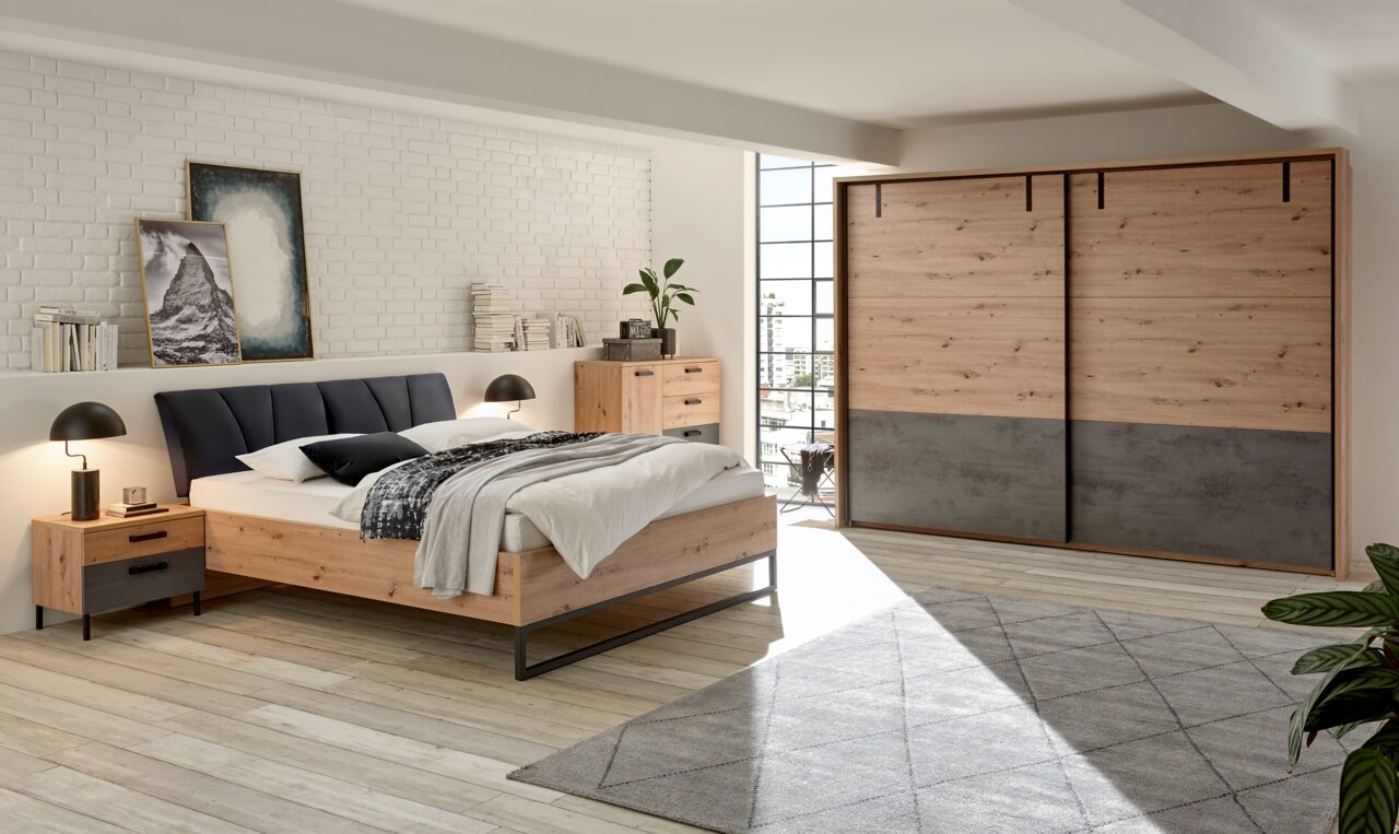 Schlafzimmeransicht mit modernem Schwebetürenschrank, Bett und Nachtkommode in Holzoptik, seitliche Perspektive.