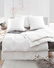 Blick auf ein Bett mit weißen Daunenkissen und Daunendecke, dekoriert mit einem grauen Fellüberwurf.