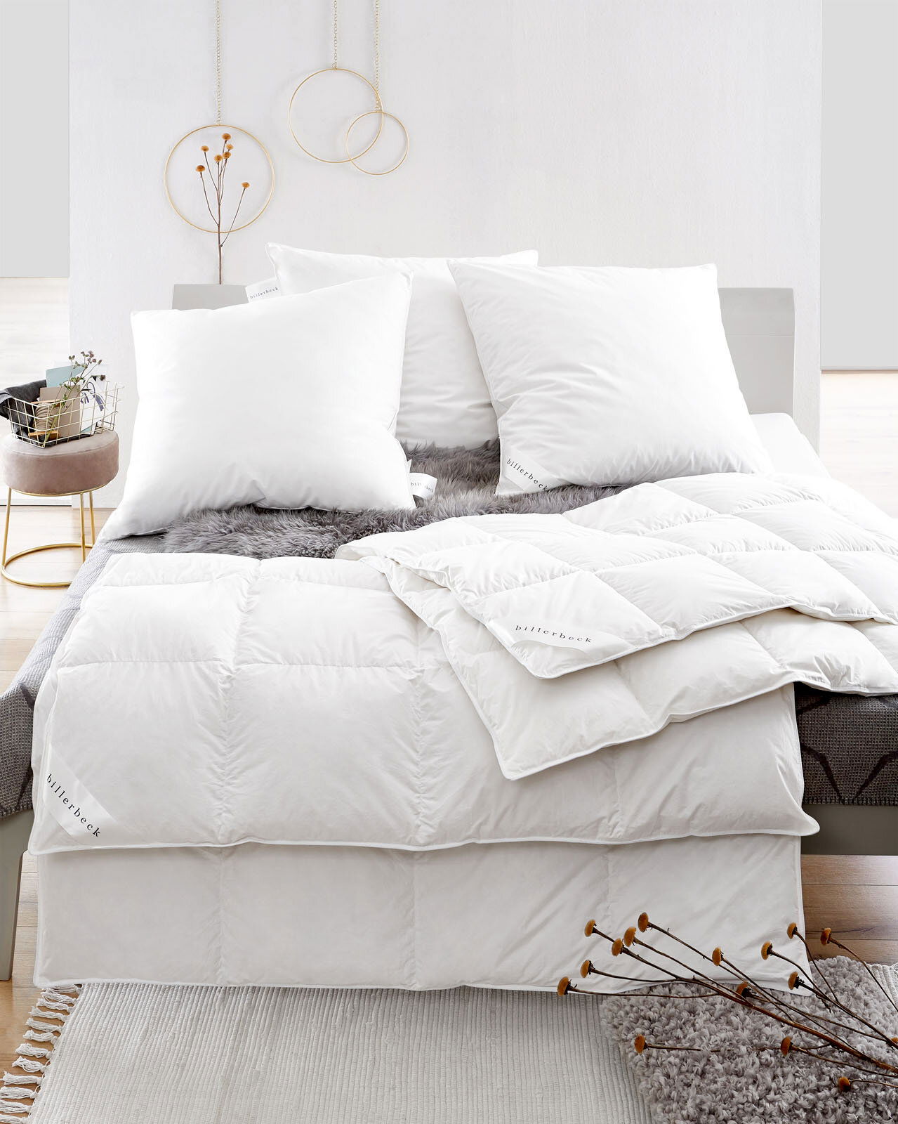 Blick auf ein Bett mit weißen Daunenkissen und Daunendecke, dekoriert mit einem grauen Fellüberwurf.