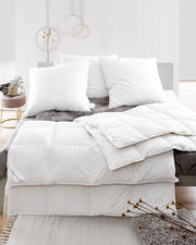 Blick auf ein Bett mit weißen Daunenkissen und Daunendecke, dekoriert mit einem grauen Fellüberwurf.