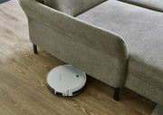 Ein graues Sofa auf einem Holzboden, darunter ein weißer Saugroboter. Perspektive von oben.