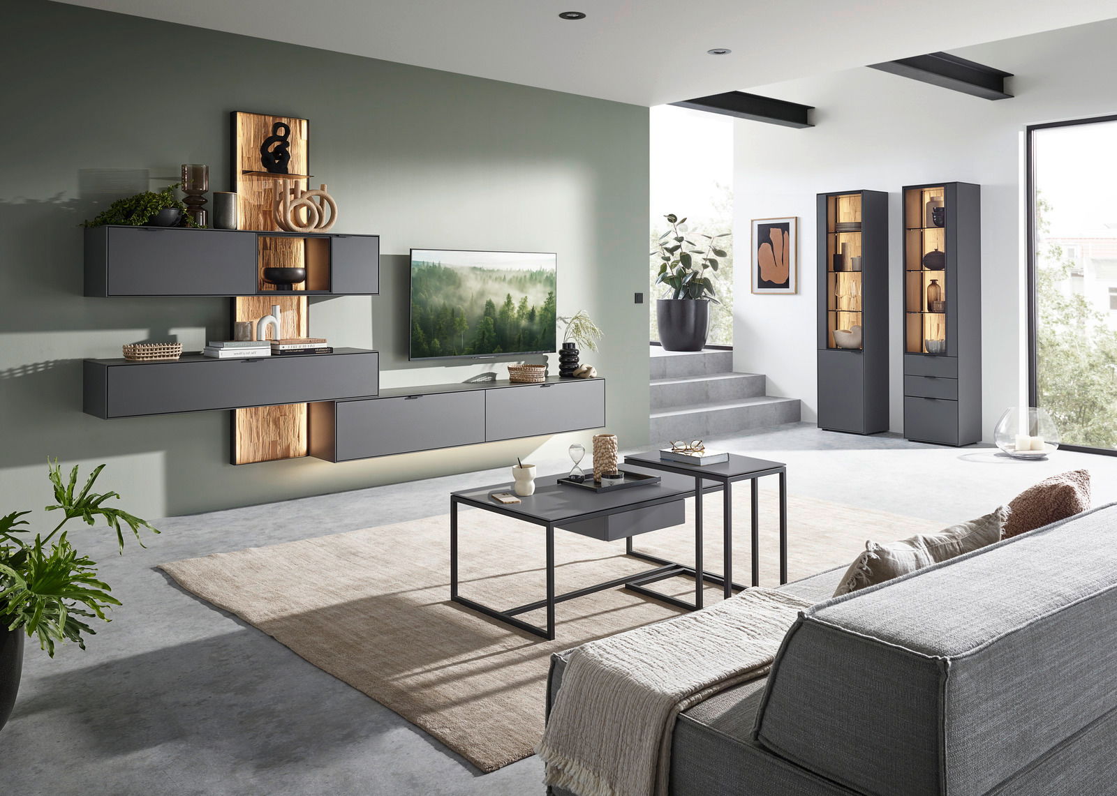 Moderne Wohnzimmer-Wandkombination in dunklem Grau mit Holzakzenten, bestehend aus mehreren Hängeschränken und einem TV-Board, stilvoll dekoriert. Perspektive von der Seite mit Blick auf die gesamte Wohnwand.