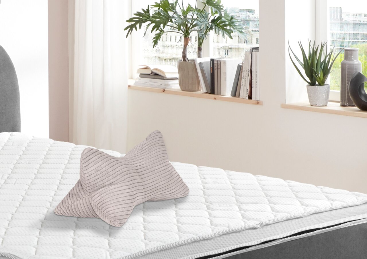 Leseknochen in hellgrauer Farbe mit Streifenmuster, auf einem weißen Bett liegend, seitliche Perspektive