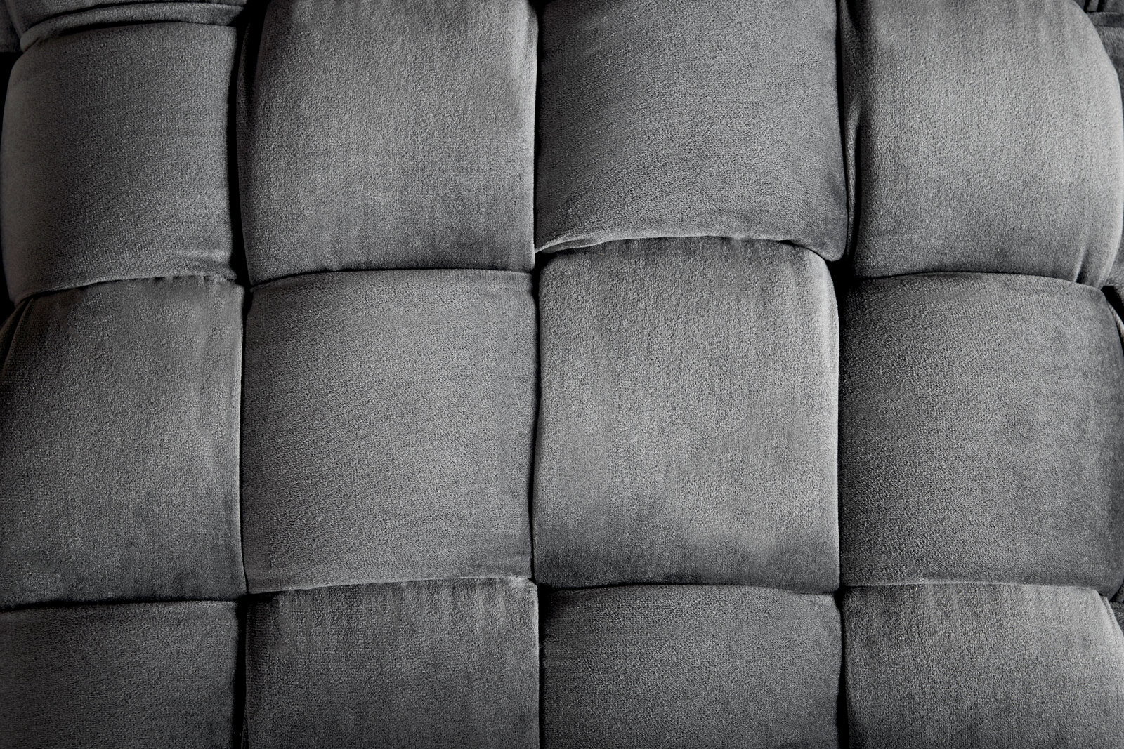 Nahaufnahme eines grauen, gepolsterten Hockers mit quadratischem Muster, von oben betrachtet.