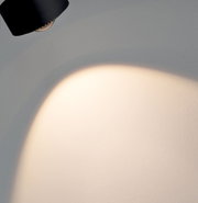 Schienenspot Aldan in schwarzer Farbe, an der Decke montiert, mit einem Lichtstrahl auf eine Wand gerichtet, seitliche Perspektive.