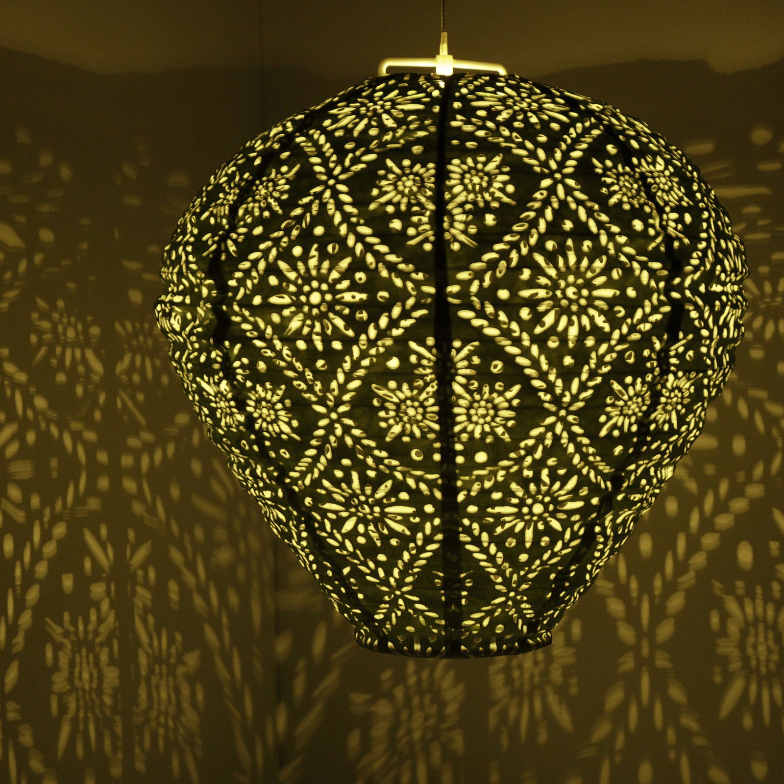 Hängende Solar Laterne mit filigranem Muster, das ein dekoratives Licht- und Schattenspiel an die Wand wirft, seitliche Perspektive.