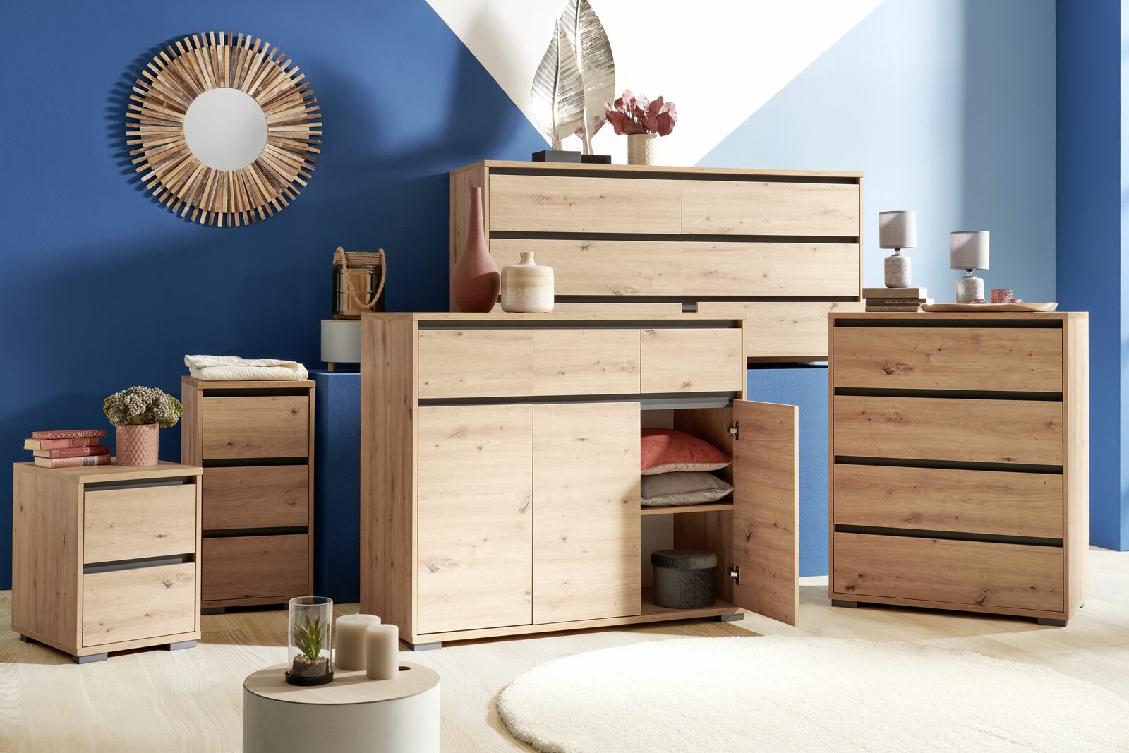 Moderne Holzkommoden in verschiedenen Größen, frontal fotografiert, vor einer blauen Wand mit dekorativem Spiegel.