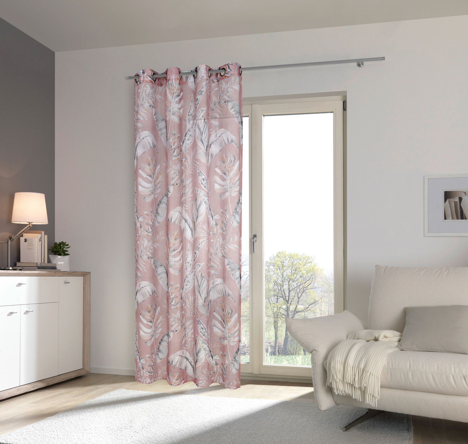 Rosa Vorhang mit tropischem Blattmuster, aufgehängt an einer Gardinenstange vor einem Fenster, seitliche Perspektive.