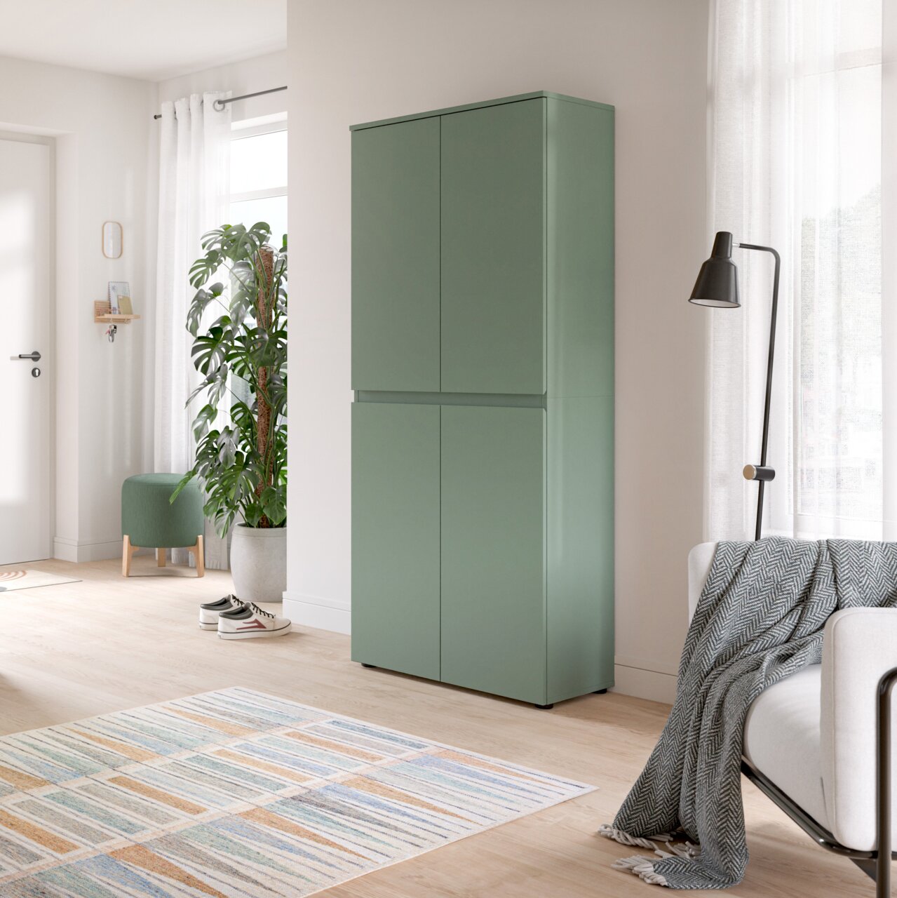 Grüner, minimalistischer Hochschrank mit vier grifflosen Türen in einem hellen Wohnraum, gezeigt in leichter Schrägansicht von vorn rechts.