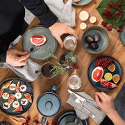 Vogelperspektive auf ein stilvolles Frühstücks-Set in Denim-Blau mit Tellern, Tassen und Schalen, dekoriert mit frischen Früchten und Kerzen auf einem Holztisch.