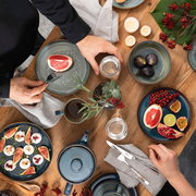 Vogelperspektive auf ein stilvolles Frühstücks-Set in Denim-Blau mit Tellern, Tassen und Schalen, dekoriert mit frischen Früchten und Kerzen auf einem Holztisch.