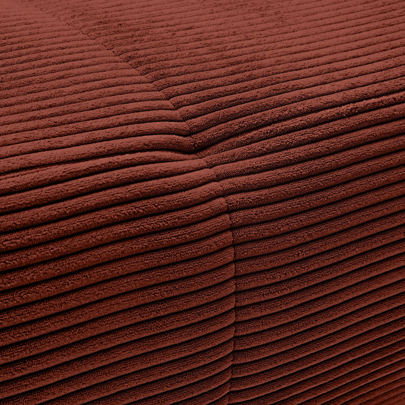 Nahaufnahme einer rotbraunen, gerippten Stoffoberfläche mit sichtbarer Naht.