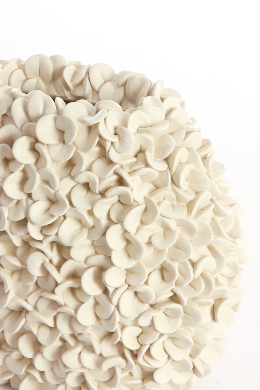 Close-up van een witte vaas met een bloembladachtige structuur, gezien vanaf de zijkant.