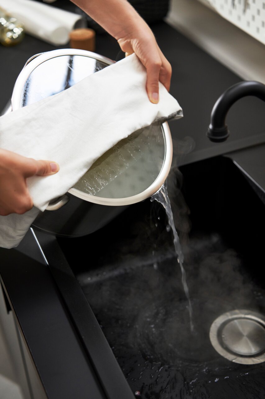 5-delige pannenset True Flow in de keuken, water wordt uit een pan in de gootsteen gegoten, zijaanzicht