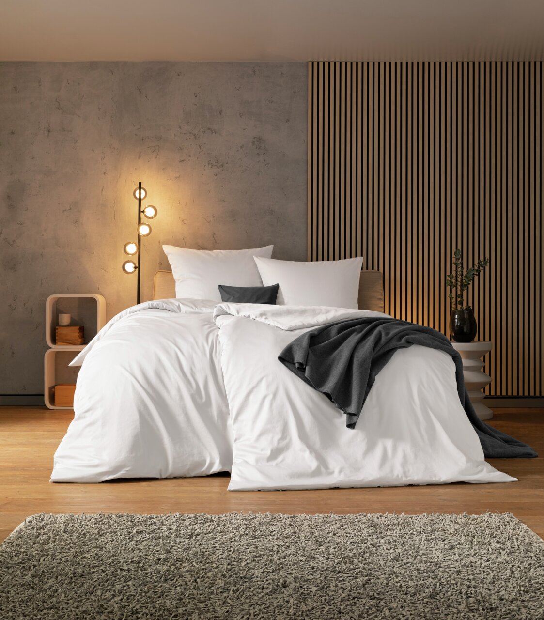 Gezellige slaapkamer met modern wit beddengoed, versierd met grijze kussens en een deken, gefotografeerd vanuit het vooraanzicht.