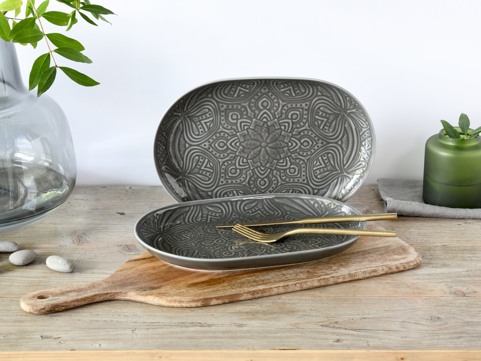 creaTable Servierteller-Set 2-tlg ORIENT MANDALA Grauer ovaler Keramikteller mit Mandala-Prägung, dekorativ auf Holzbrett mit goldfarbenem Besteck arrangiert, perspektivisch in leicht schräger Frontansicht