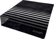 Gestreifte JOOP! Wohndecke in Schwarz-, Grau- und Weißtönen mit eingewebtem Logo, schräg von oben in Perspektive fotografiert; eine Ecke ist umgeschlagen und zeigt die Rückseite.