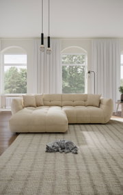 Beige Ecksofa in einem hellen Wohnzimmer mit großen Fenstern, zwei Kissen und einer schlafenden Katze auf einem Teppich. Perspektive von vorne.
