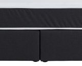 Nahaufnahme eines Boxspringbettes in dunklem Stoff mit weißem Rand, Vorderansicht.