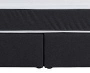 Nahaufnahme eines Boxspringbettes in dunklem Stoff mit weißem Rand, Vorderansicht.