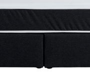 Nahaufnahme eines Boxspringbettes in dunklem Stoff mit weißem Rand, Vorderansicht.