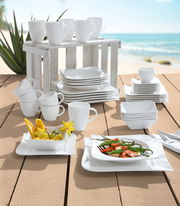 Kombiservice 42-teilig Melodie, bestehend aus weißen Tassen, Tellern und Schalen, auf einem Holztisch mit Strandhintergrund präsentiert. Perspektive: seitlich von oben.