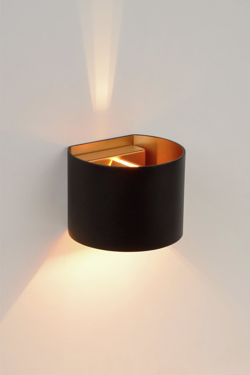 Moderne wandlamp XIO in zwart met een gouden binnenkant, die warm licht naar boven en beneden verspreidt. Zijaanzicht.