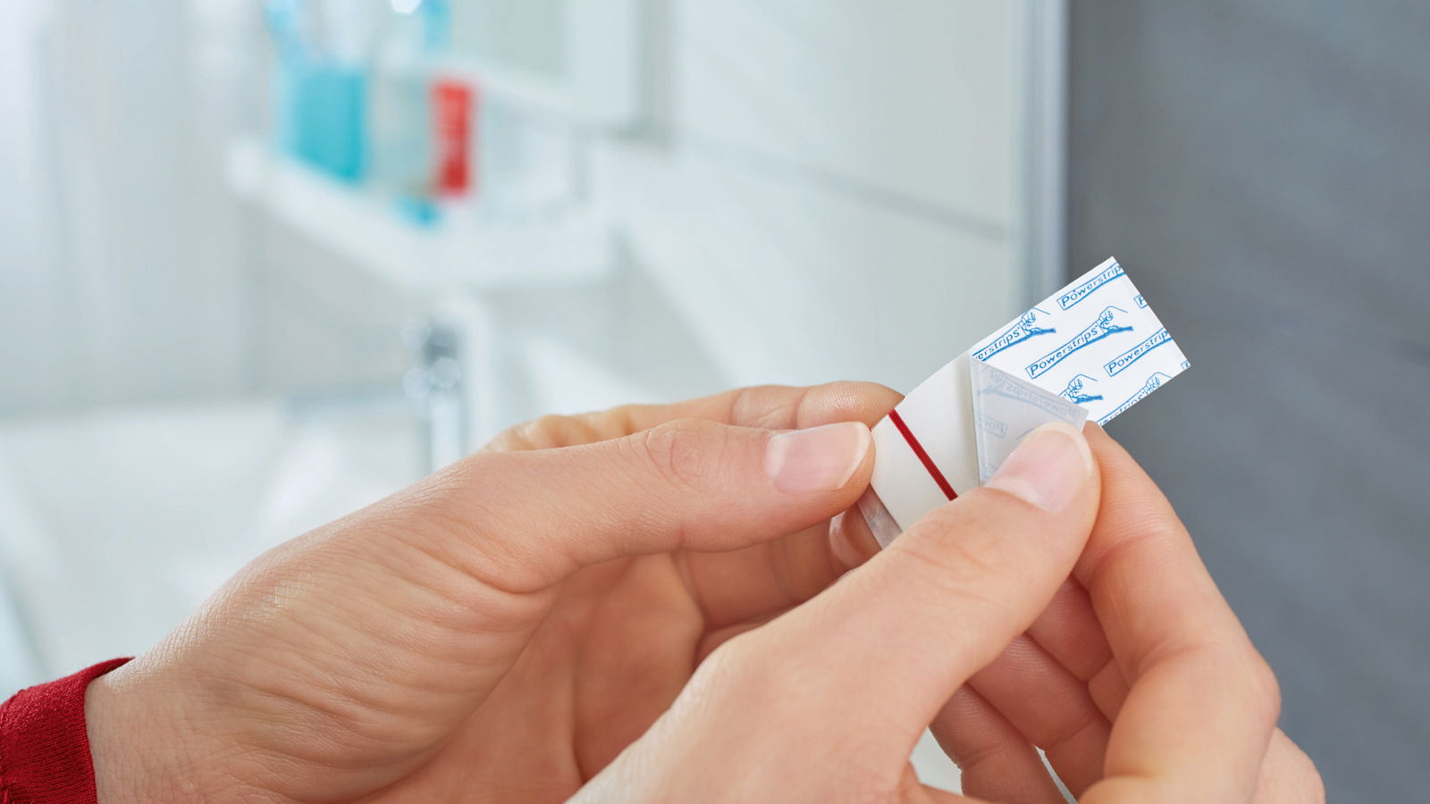 Nahaufnahme von Händen, die einen tesa Powerstrip Waterproof in einem Badezimmer halten.