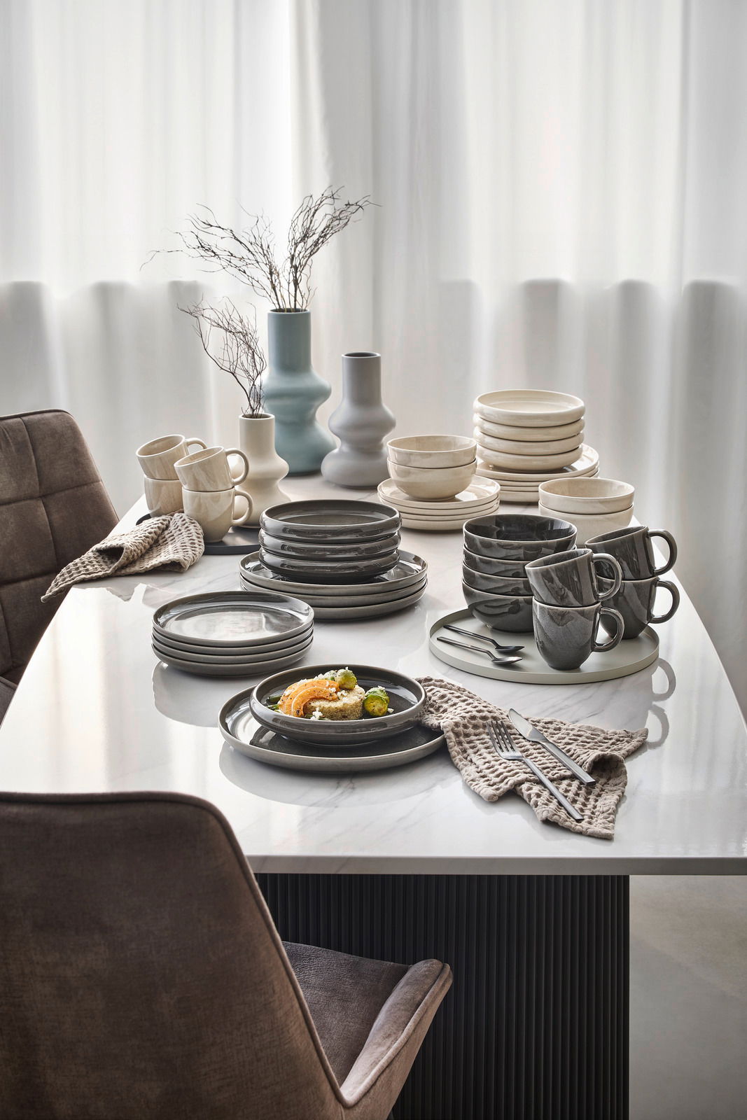 Elegantes Geschirrset in Grau- und Beigetönen auf einem Esstisch, seitliche Perspektive.