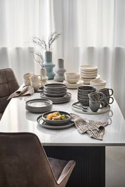 Elegantes Geschirrset in Grau- und Beigetönen auf einem Esstisch, seitliche Perspektive.