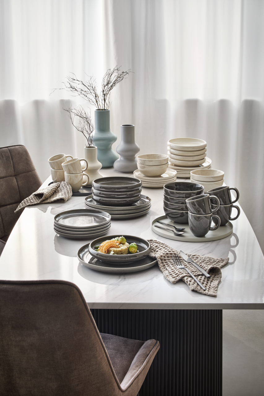Elegantes Geschirrset in Grau- und Beigetönen auf einem Esstisch, seitliche Perspektive.