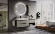 Moderner Badezimmerbereich mit rundem, beleuchtetem Flächenspiegel an der Wand, grauem Waschtisch mit Schubladen und Waschbecken, seitlicher Perspektive.
