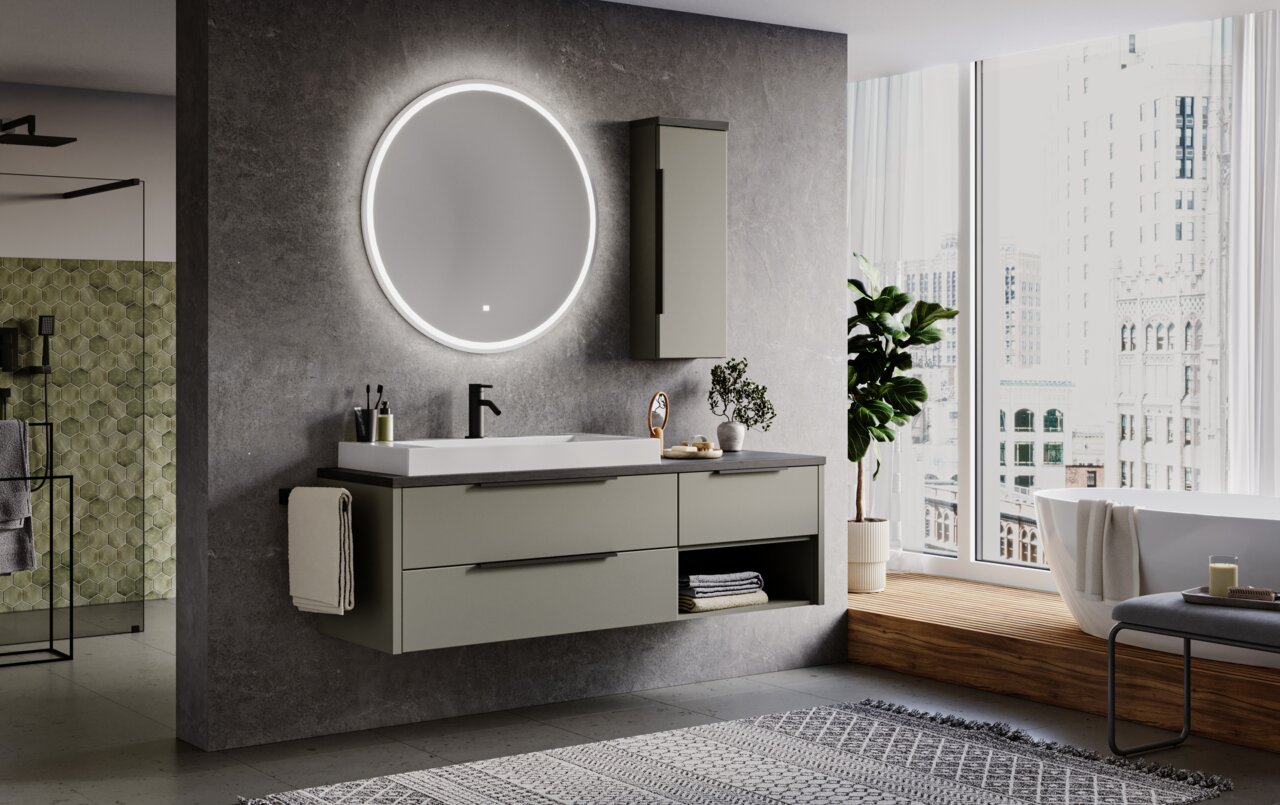 Moderner Badezimmerbereich mit rundem, beleuchtetem Flächenspiegel an der Wand, grauem Waschtisch mit Schubladen und Waschbecken, seitlicher Perspektive.