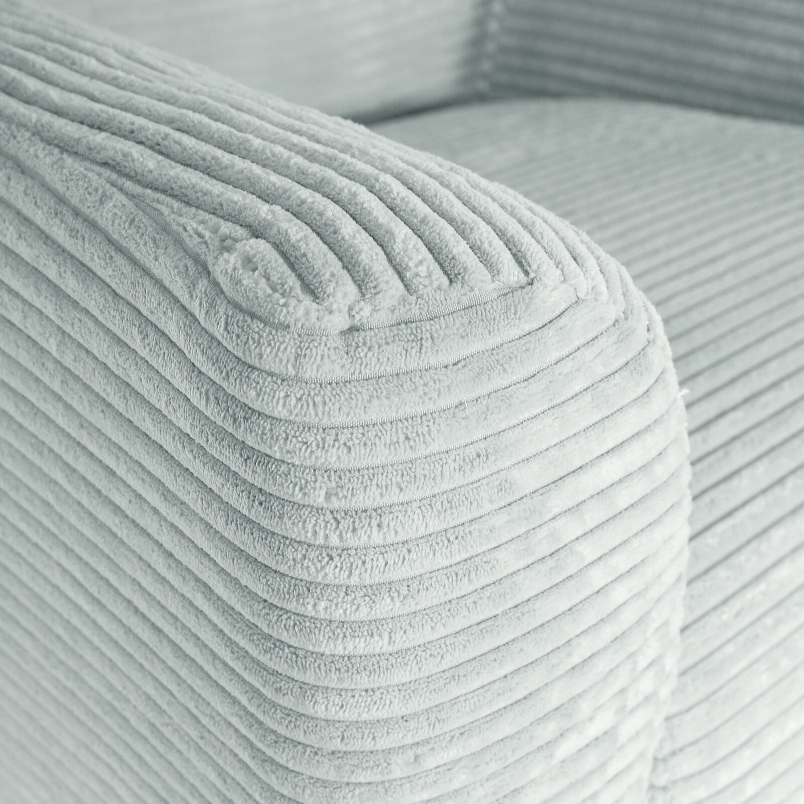 Nahaufnahme der abgerundeten Armlehne eines hellgrauen Cordstoff-Sofas mit gerippter Struktur, Perspektive: schräg von oben