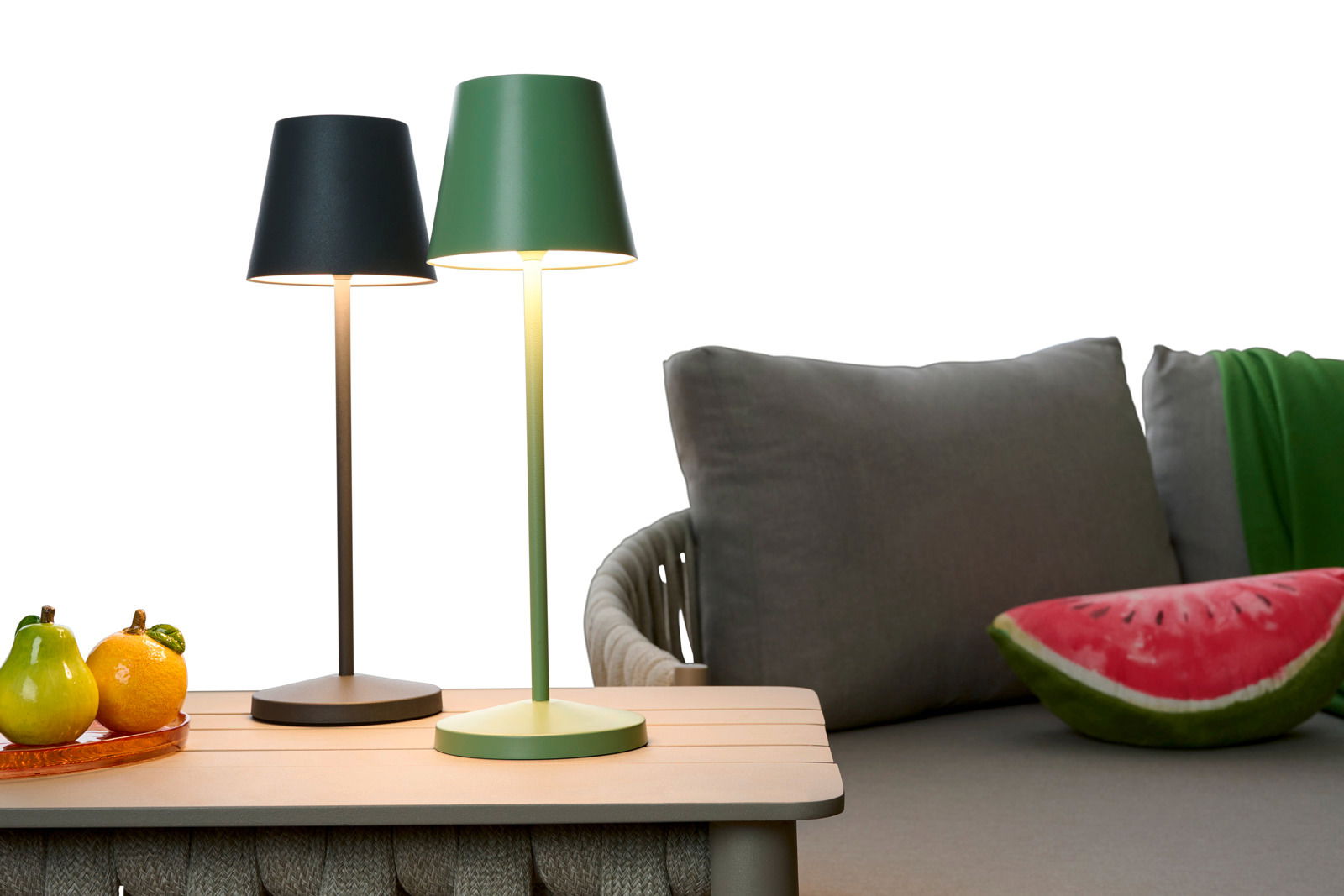 Zwei Akku-Tischleuchten in Schwarz und Grün auf einem Tisch, seitliche Perspektive, mit einem Sofa im Hintergrund.