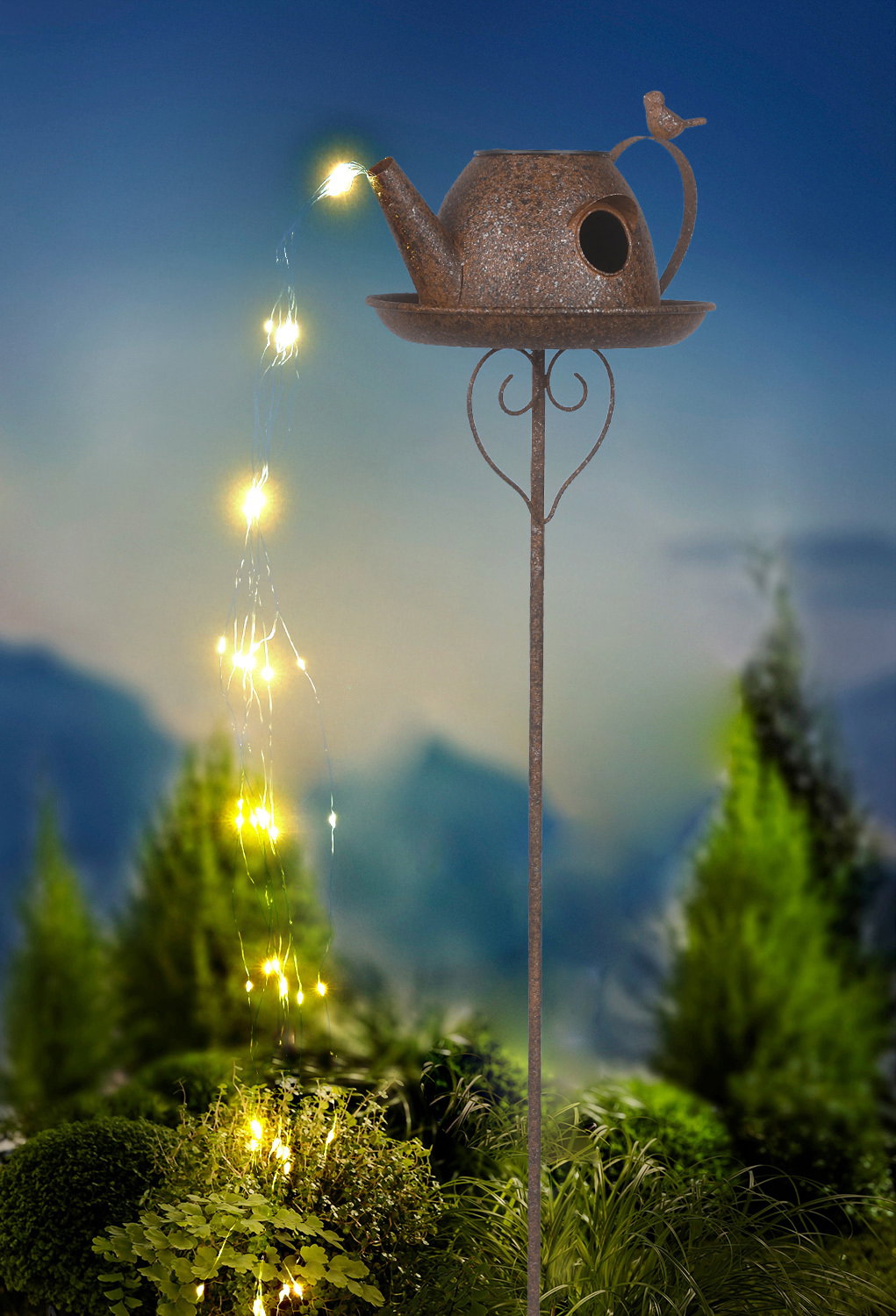 Solarleuchte in Form einer Gießkanne mit Lichterkette, die von oben nach unten fließt, auf einem Stab montiert, vor einem Hintergrund mit Pflanzen, seitliche Perspektive.