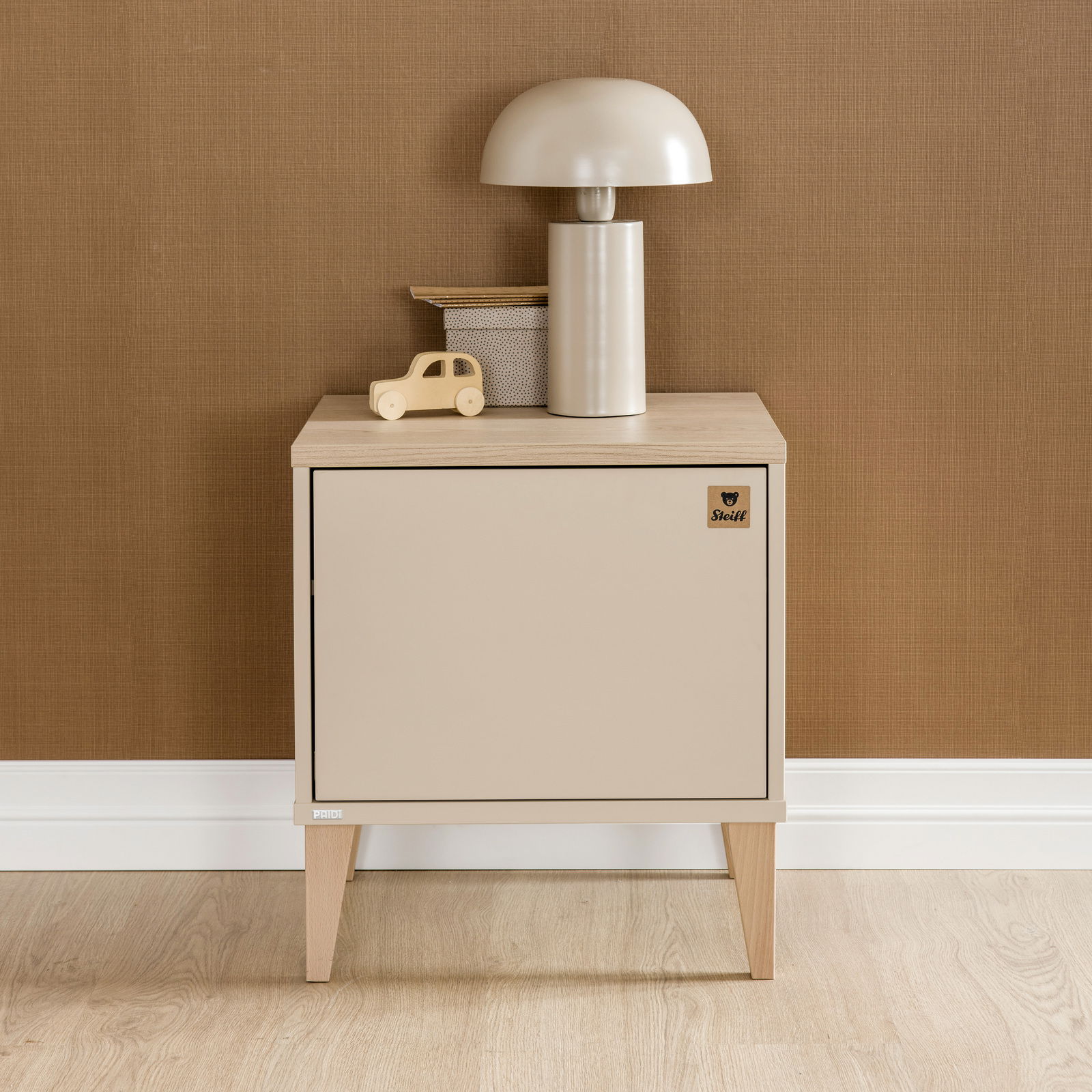 Frontale Ansicht einer modernen Nachtkonsole in Beige mit Holzbeinen, dekoriert mit einer Tischlampe und einem Spielzeugauto.