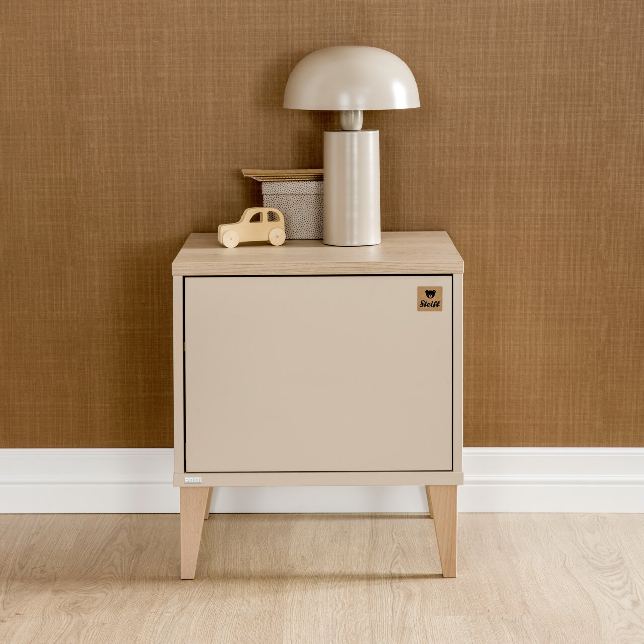 Frontale Ansicht einer modernen Nachtkonsole in Beige mit Holzbeinen, dekoriert mit einer Tischlampe und einem Spielzeugauto.