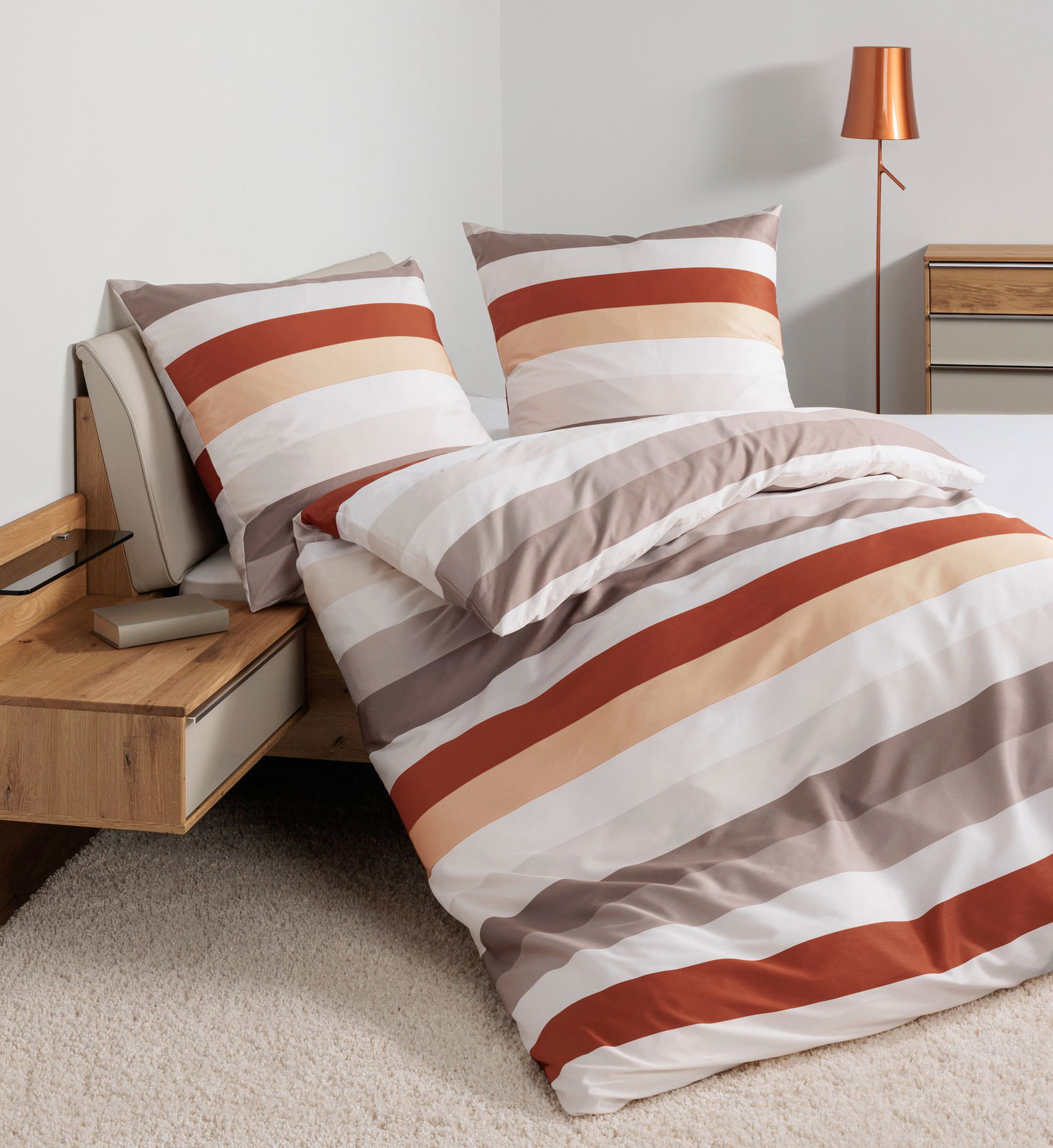 Bettwäsche-Set mit Streifenmuster in warmen Tönen auf einem Bett, seitliche Perspektive