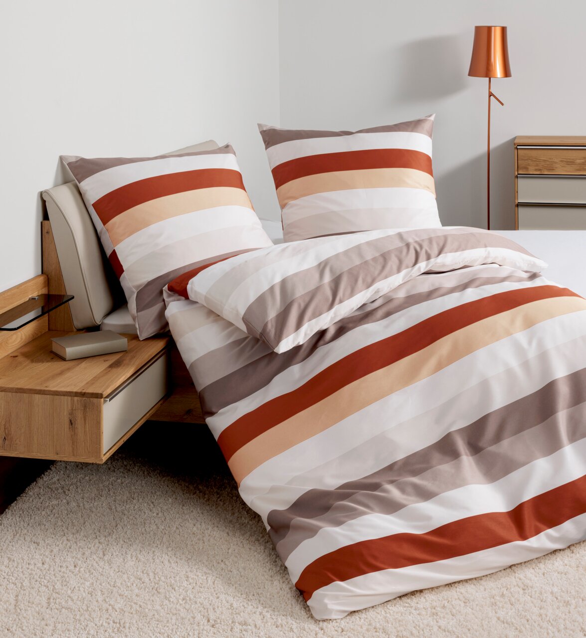 Bettwäsche-Set mit Streifenmuster in warmen Tönen auf einem Bett, seitliche Perspektive