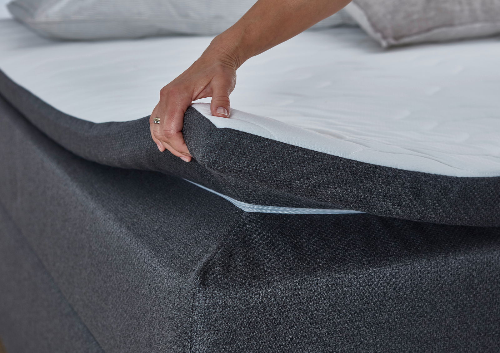 Nahaufnahme eines Boxspringbetts mit einer Hand, die die Matratze anhebt, um die Struktur und den Bezug zu zeigen.