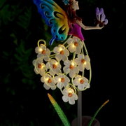 Close-up vanuit zijaanzicht: decoratieve tuinlamp op zonne-energie met een kleurrijk elfje en stralend witte bloemen tegen een donkere achtergrond