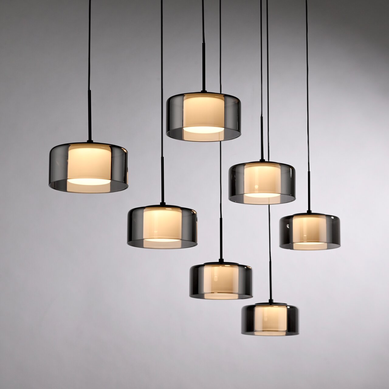 Moderne Pendelleuchte RIKA mit sieben zylindrischen, rauchgrauen Glasschirmen, von unten fotografiert.