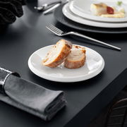 Weißer Brotteller NewMoon 16cm mit zwei Brotscheiben, seitliche Perspektive auf einem gedeckten Tisch.