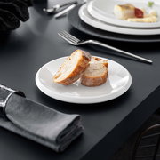 Weißer Brotteller NewMoon 16cm mit zwei Brotscheiben, seitliche Perspektive auf einem gedeckten Tisch.