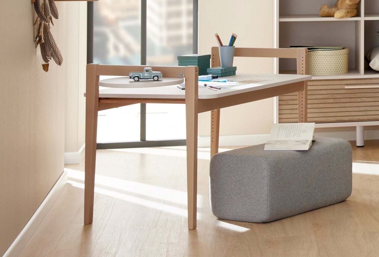 Het tafelblad van de Tiny Table in een moderne ruimte, gezien vanaf de zijkant, met een speelgoedautootje en schrijfspullen erop.