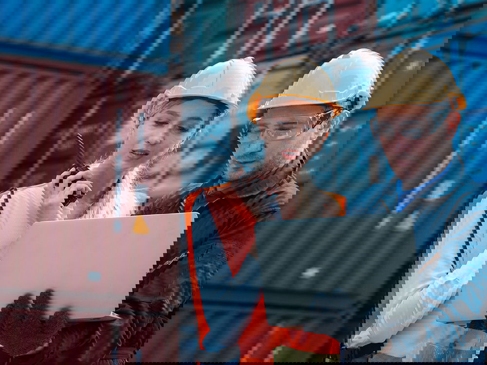 Mitarbeiter im Lager prüfen Lieferdaten mit Laptop vor Containern