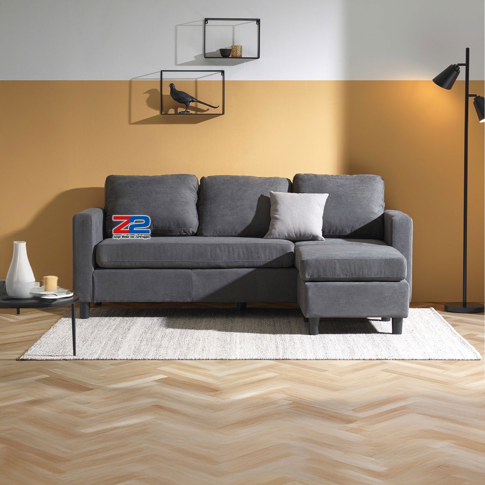 Graues Ecksofa in modernem Wohnzimmer mit gelber Wand, Teppich, Stehlampe und Wandregalen